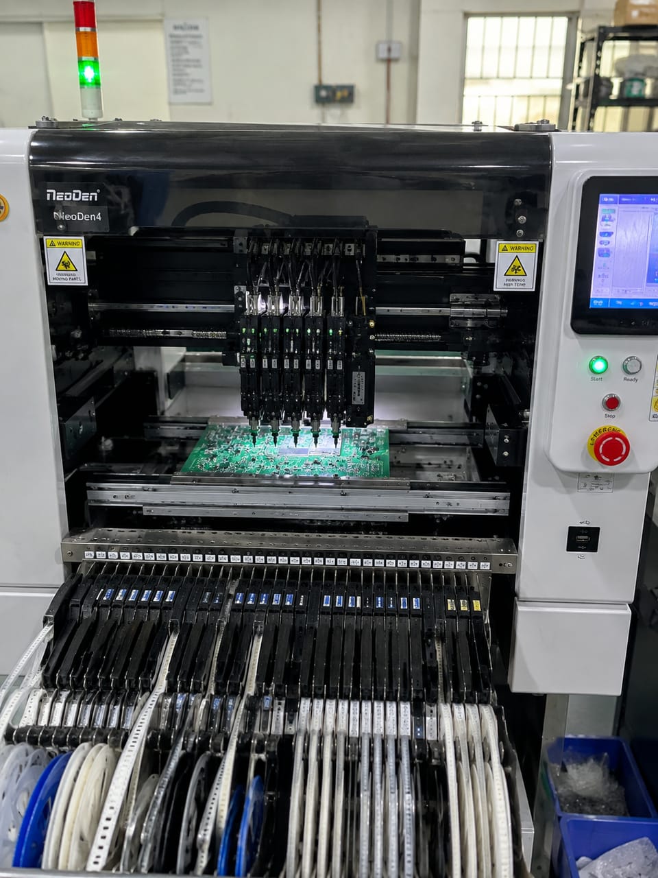 Surface-mount pick-and-place machine mid-run, component feeders loaded along the front